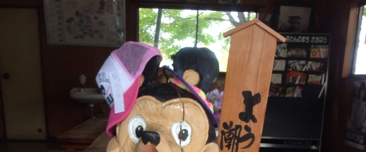 A wooden sculpture of a bear wearing a hat, sitting on a stool with the words "WELCOME" and "COME" written on it.