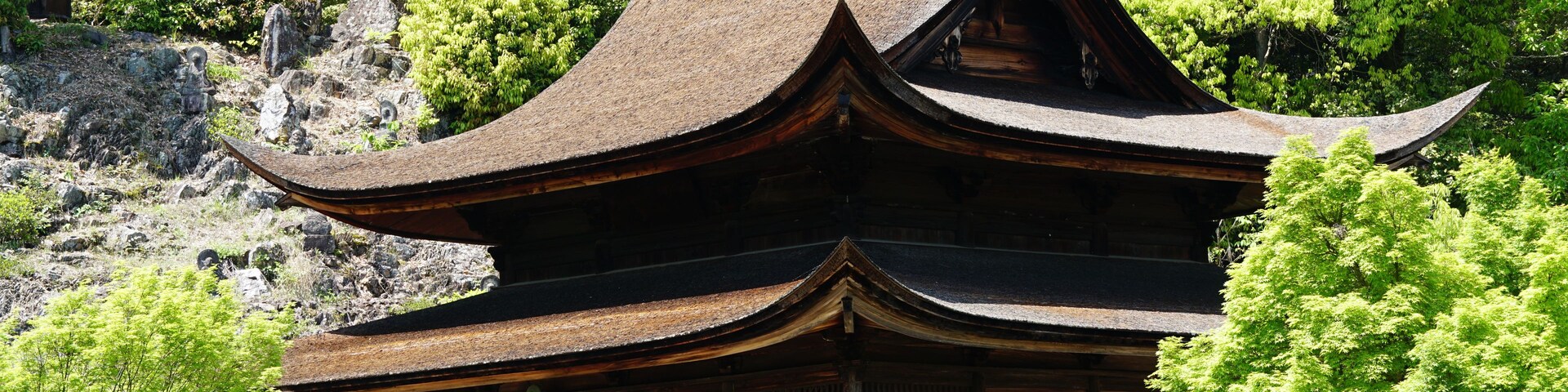 Una pagoda japonesa tradicional con varios niveles, rodeada de frondosos árboles verdes y un promontorio rocoso.