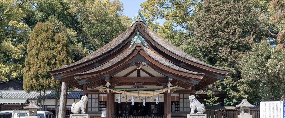 A traditional Japanese temple with a curved roof, stone lanterns, and a wooden fence.