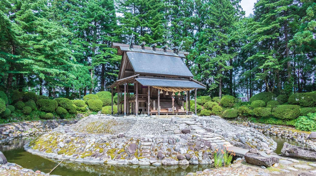 Een traditioneel Japans gebouw met een pannendak, omringd door een stenen vijver en weelderige begroeiing.