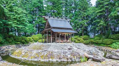 A traditional Japanese building with a tiled roof, surrounded by a stone pond and lush greenery.