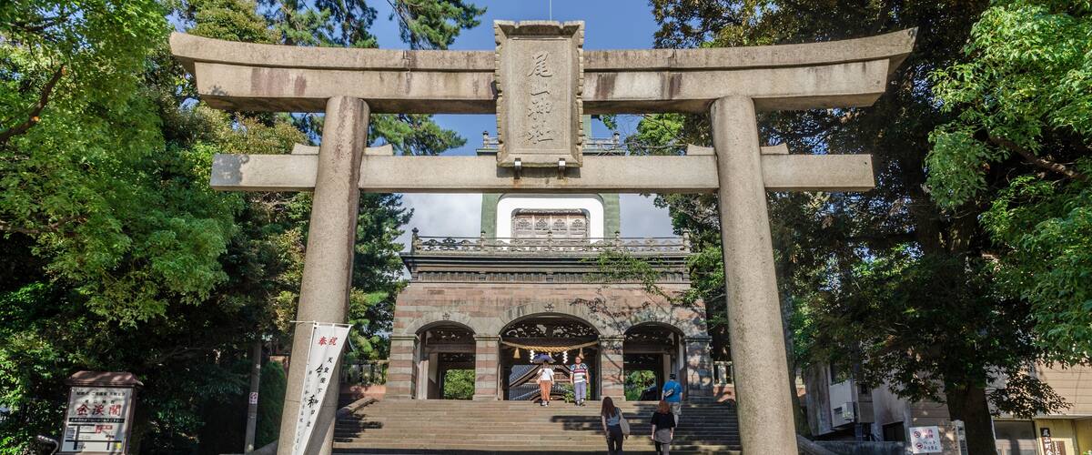 A stone torii gate with a staircase leading to a traditional building.