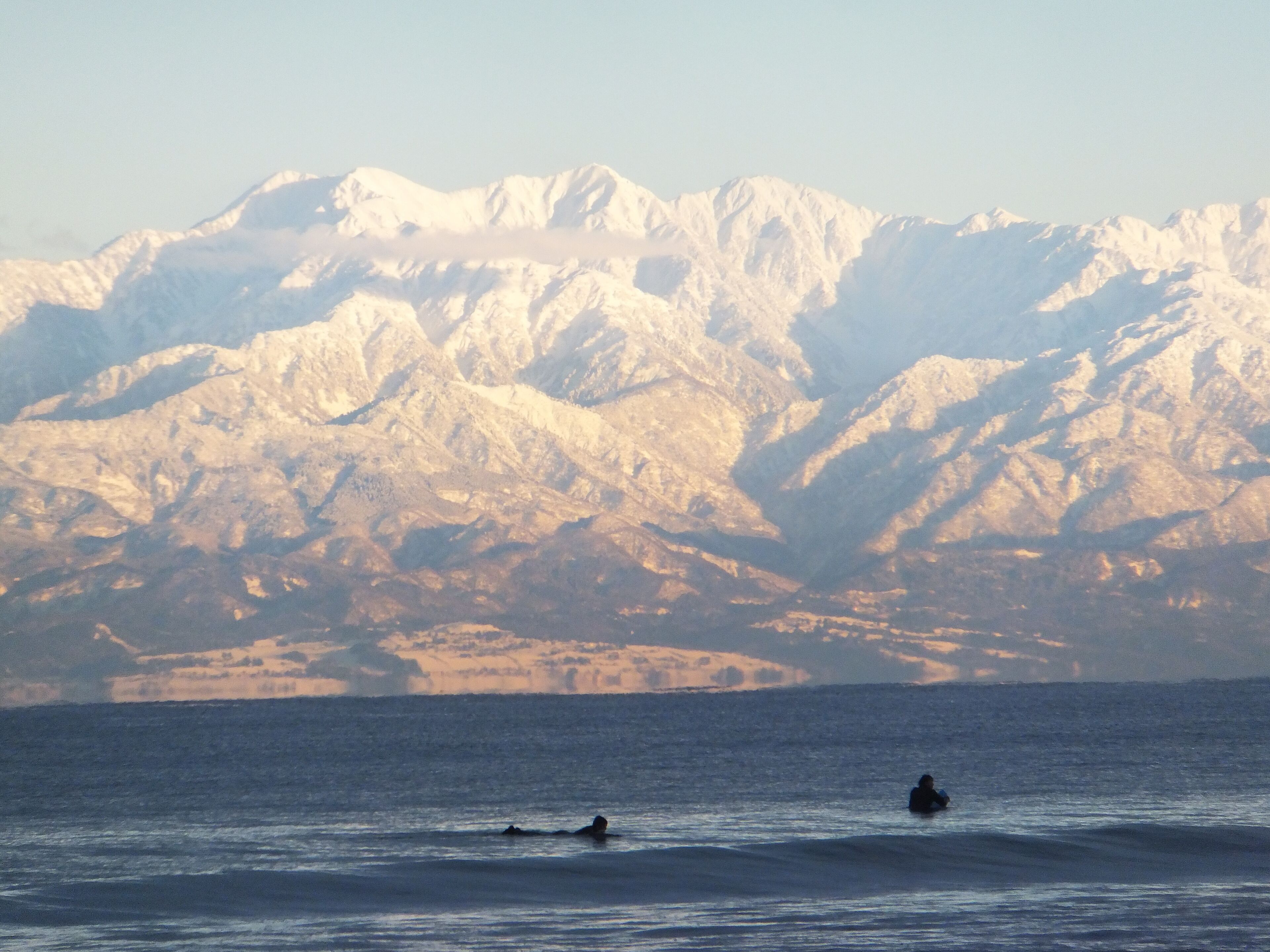 A mountainous landscape with snow-capped peaks in the background and two people swimming in the foreground.