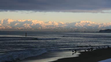 Une plage avec des vagues, une chaîne de montagnes lointaine et un ciel nuageux.