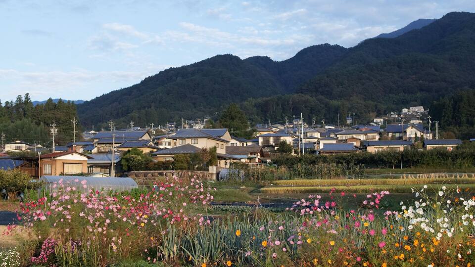 A rural village with houses, a river, and mountains in the background.