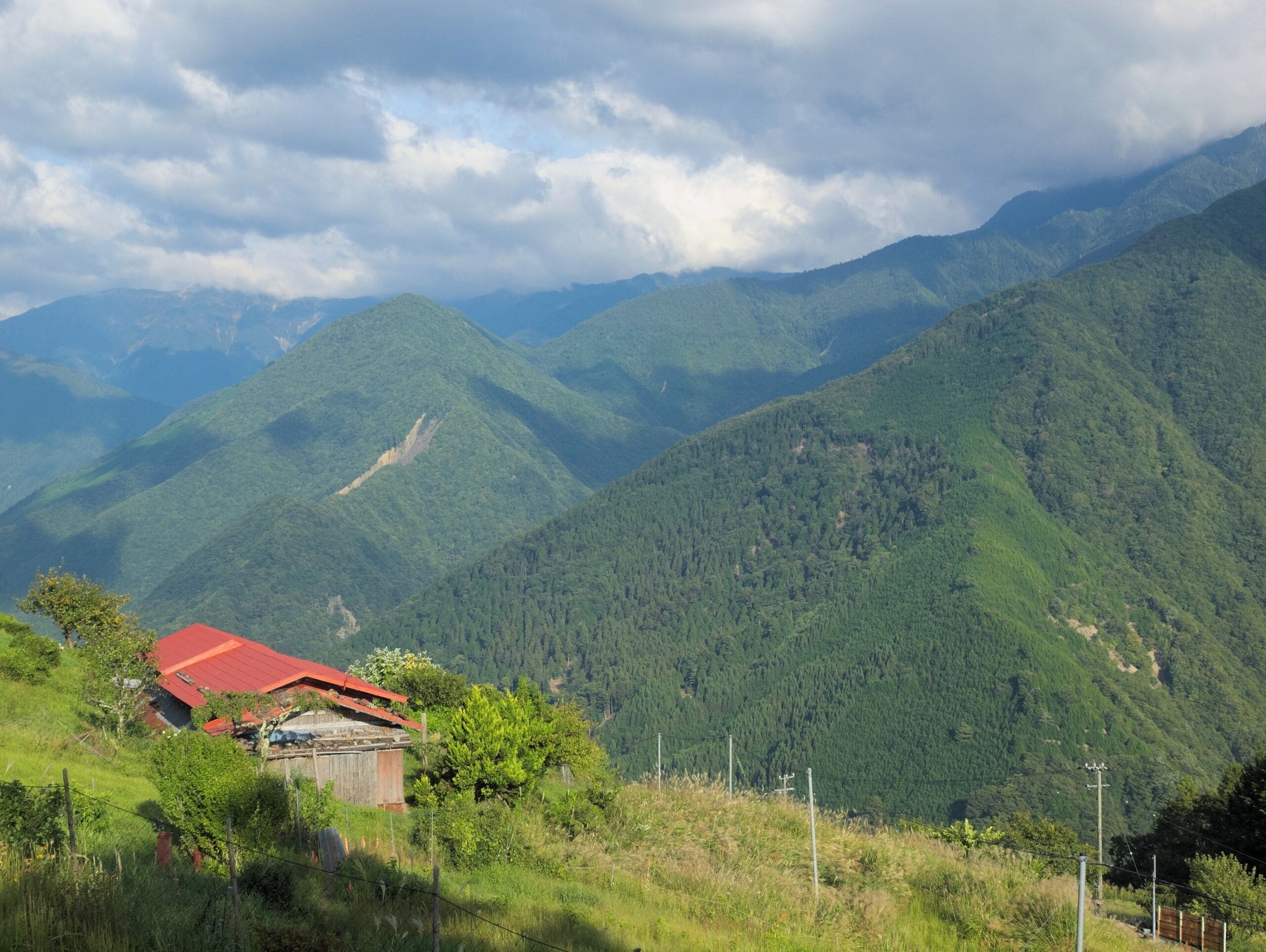 A mountainous landscape with a house on a hill and a forested valley.