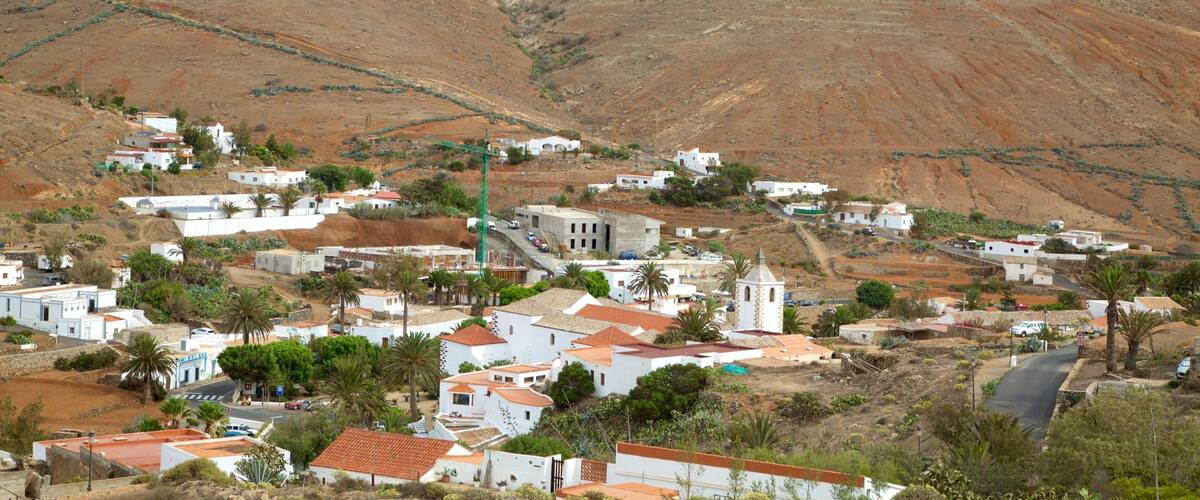 A coastal village with white buildings, a church, and a hillside.