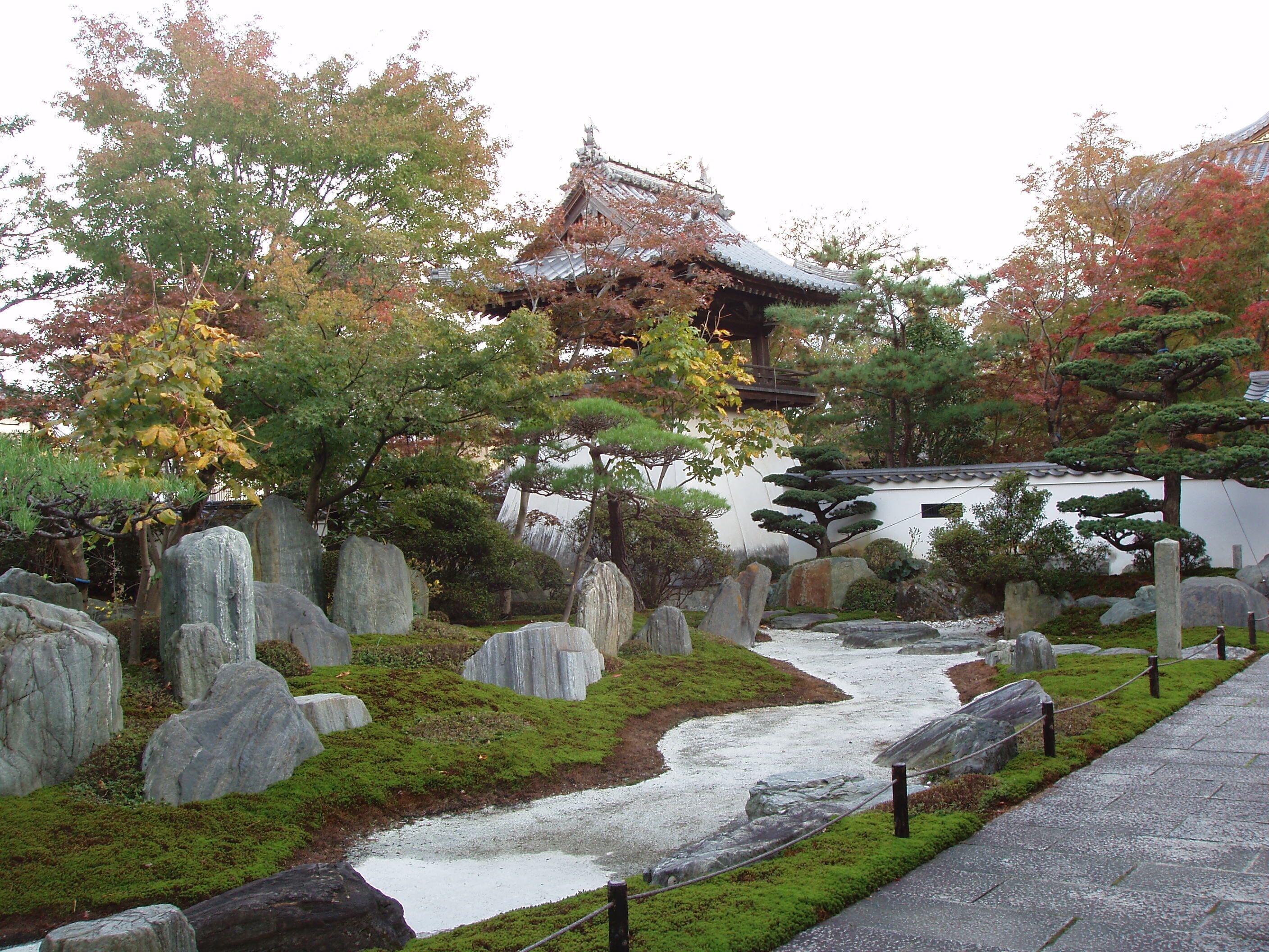 Un jardín japonés tradicional con un puente de piedra, un estanque de carpas y una pagoda.