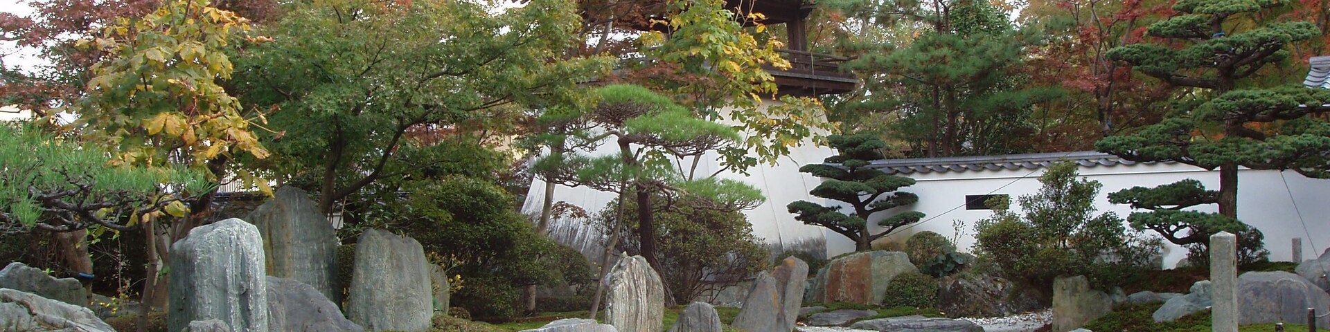 Un jardín japonés tradicional con un puente de piedra, un estanque de carpas y una pagoda.