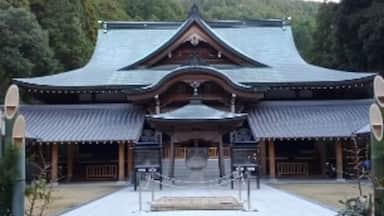 Um templo japonês tradicional com telhado curvo, colunas de madeira e um caminho de pedra que leva à entrada.