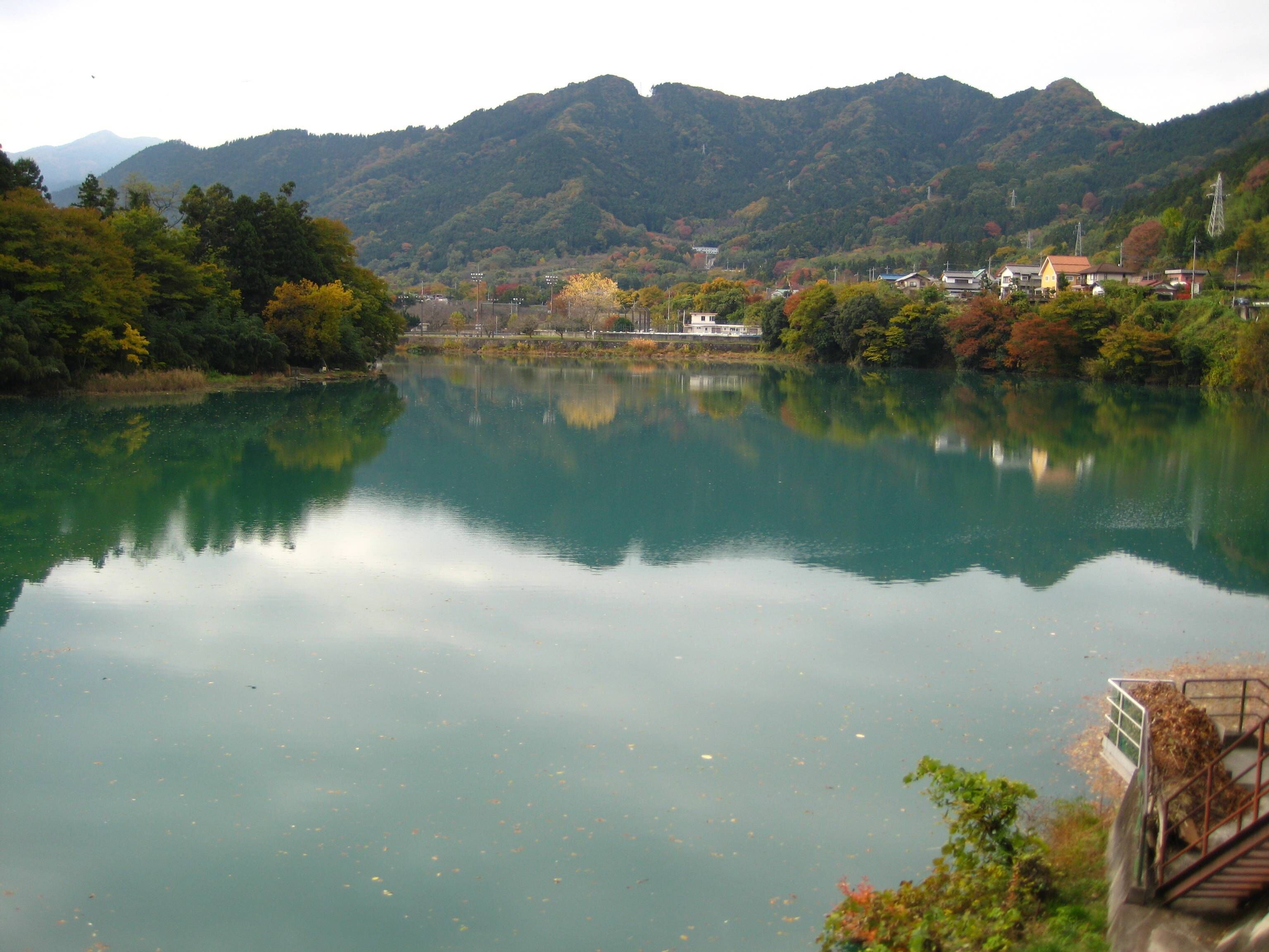 A calm lake with a mountain backdrop, surrounded by trees and buildings.