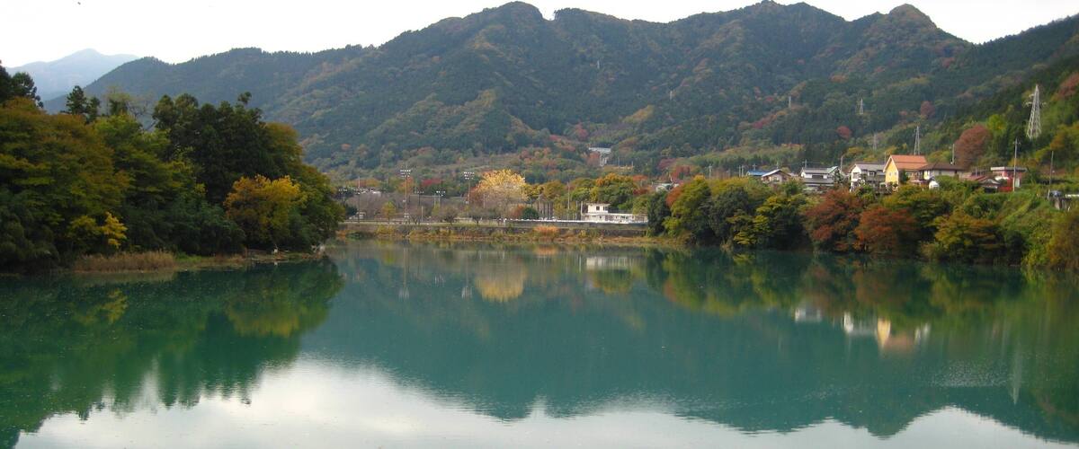 A calm lake with a mountain backdrop, surrounded by trees and buildings.