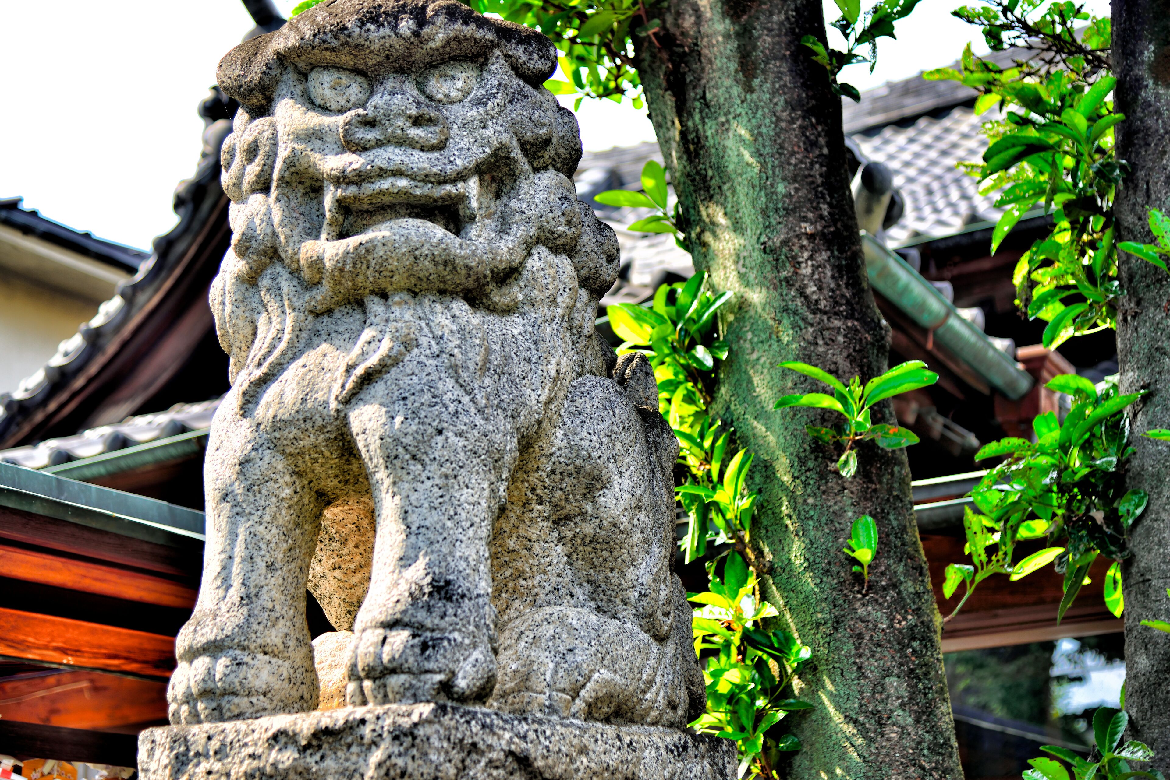 A stone lion statue in a garden with traditional tiled roofs and green foliage.