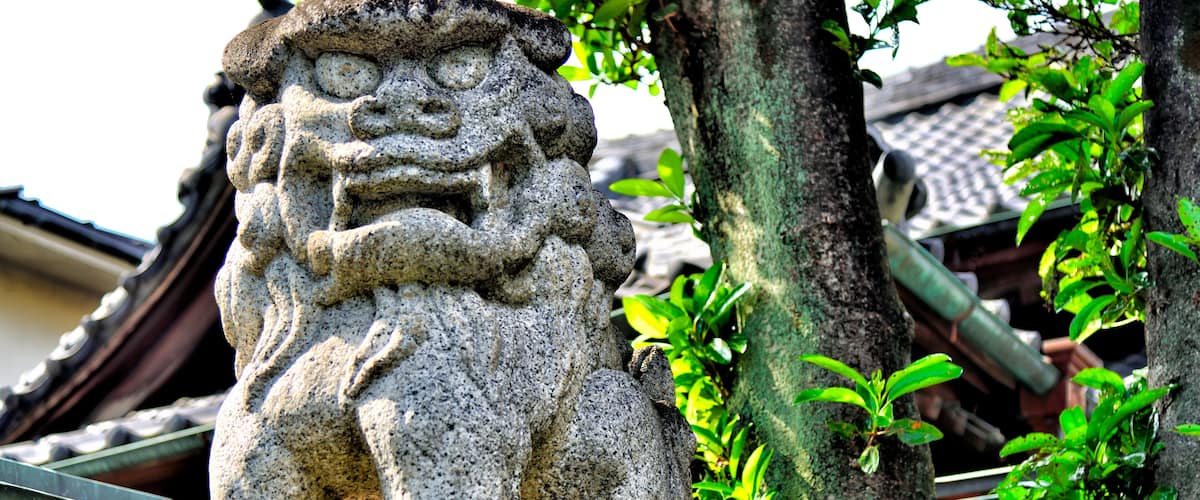 A stone lion statue in a garden with traditional tiled roofs and green foliage.