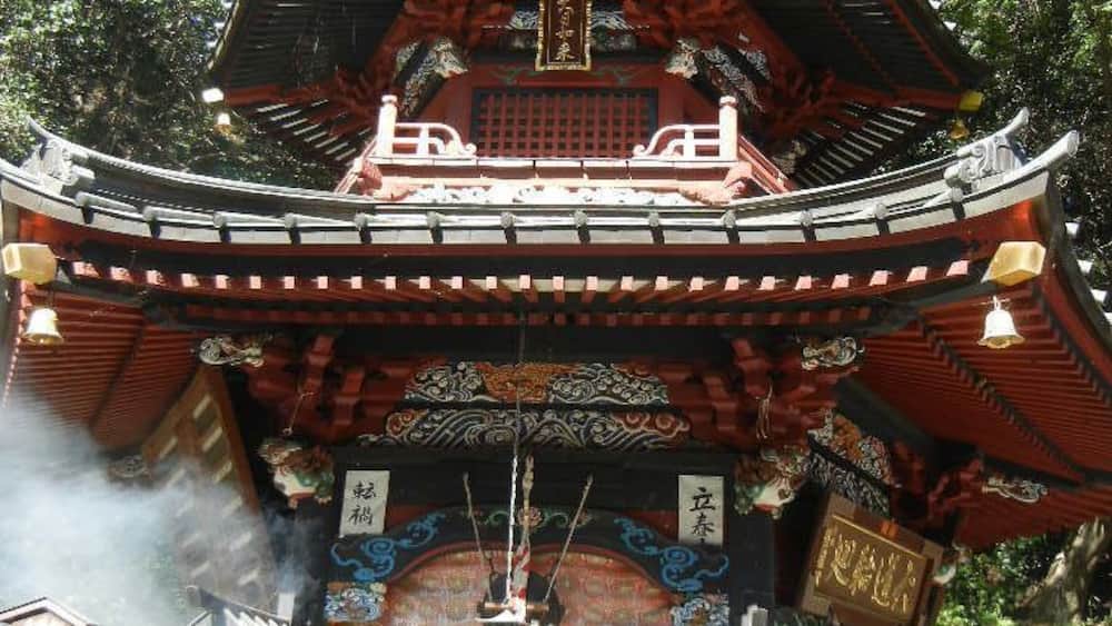 Eine traditionelle japanische Pagode mit aufwendigen Holzschnitzereien und einem Glockenturm, aus dem Rauch aufsteigt.
