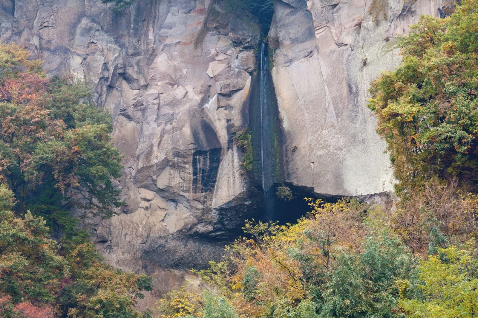 A waterfall cascading down a rocky cliff surrounded by autumn foliage.