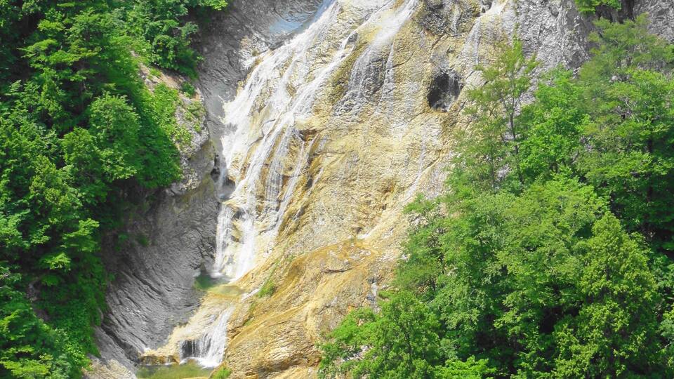 A waterfall cascading down a rocky cliff surrounded by lush green forest.