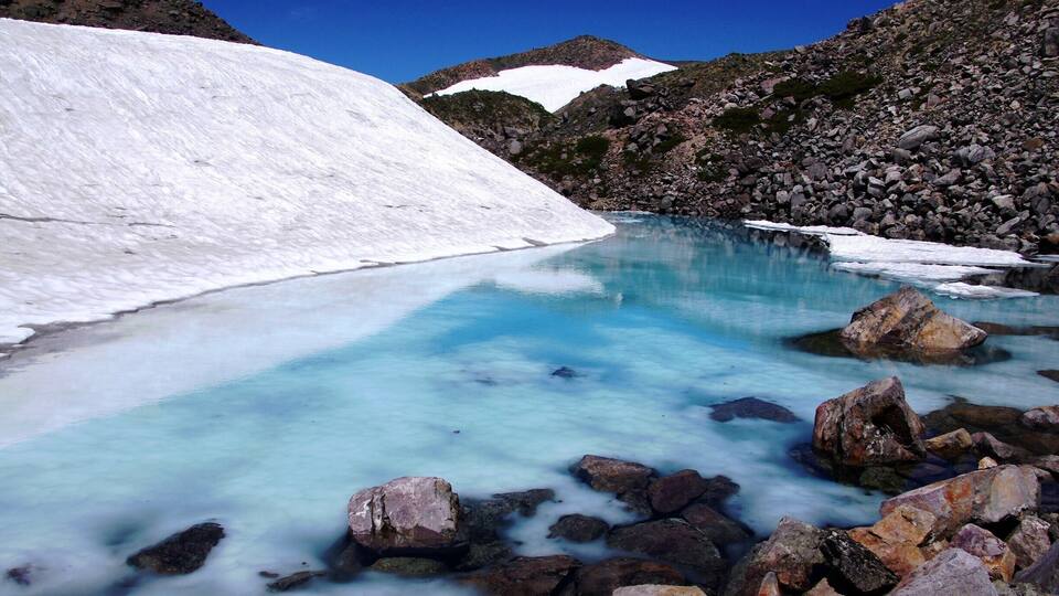 A glacier-fed lake surrounded by rocky terrain and snow-covered peaks.