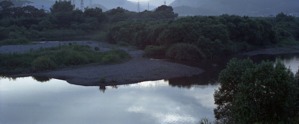 A calm river with surrounding greenery and distant mountains.