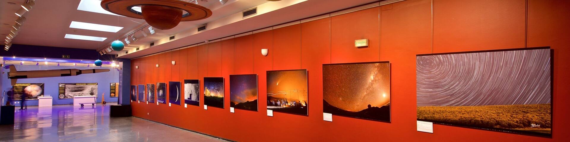 Un pasillo de museo con una serie de modelos planetarios e imágenes de cielo estrellado en la pared.