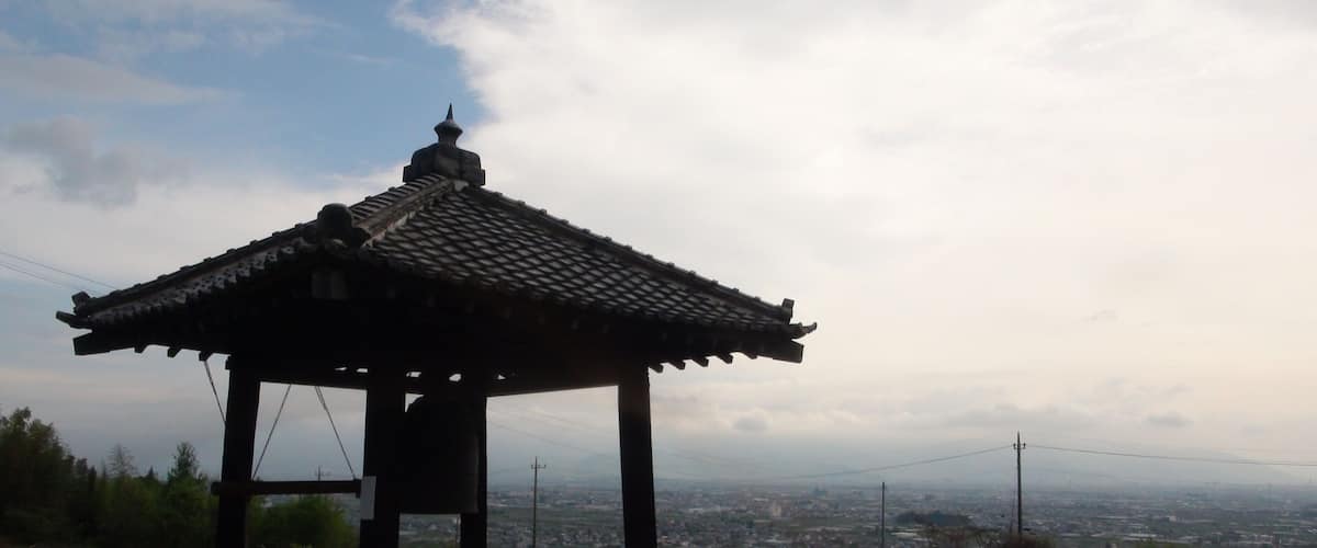 A traditional pavilion with a tiled roof, situated on a grassy hill overlooking a cityscape.