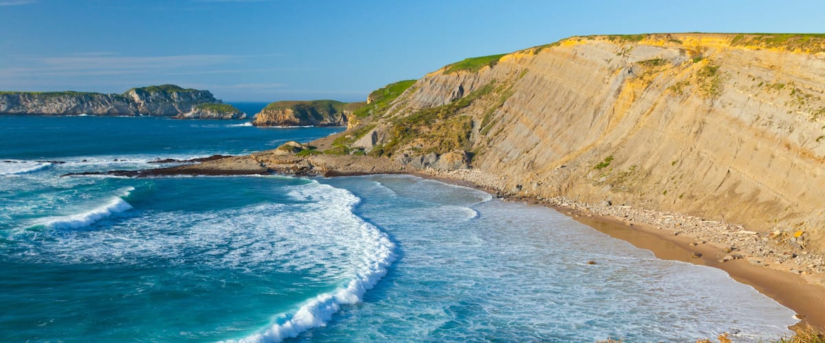 A coastal landscape with cliffs, a sandy beach, and the ocean.