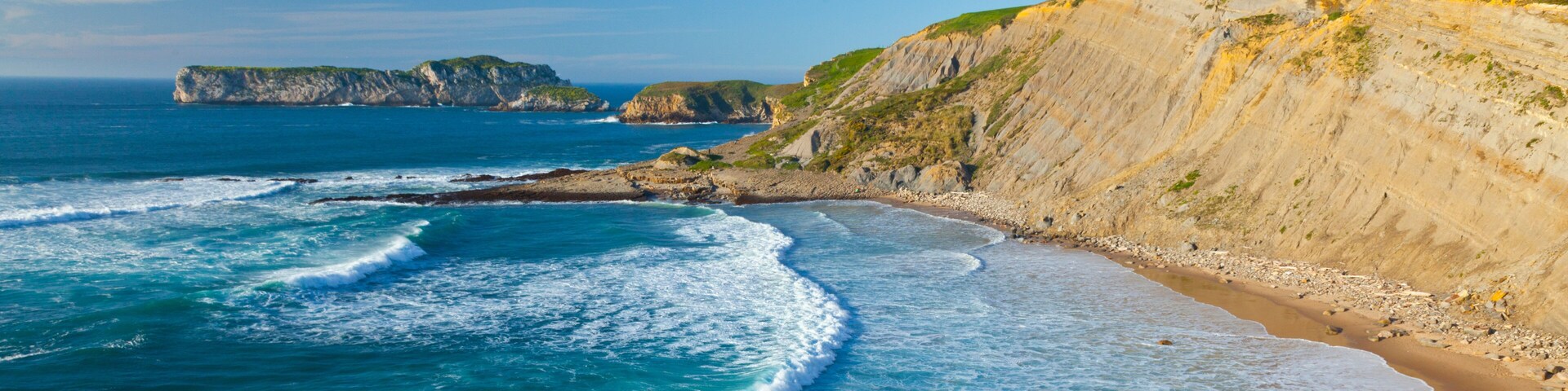 A coastal landscape with cliffs, a sandy beach, and the ocean.