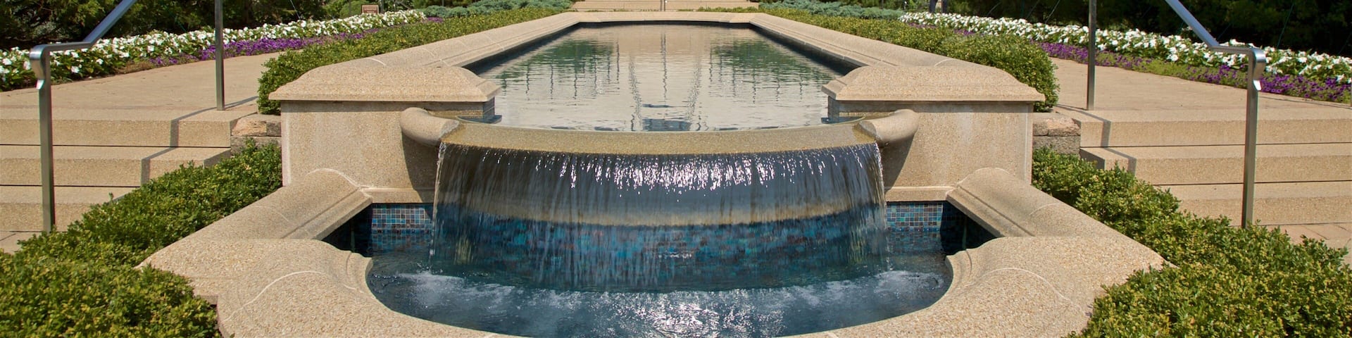 A large white building with intricate architecture, a central fountain, and a symmetrical garden with trees and flowers.