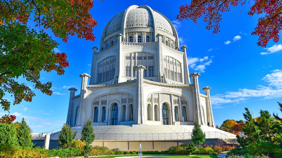 A large, ornate building with a dome and intricate architectural details, surrounded by a well-maintained garden and trees with autumn foliage.