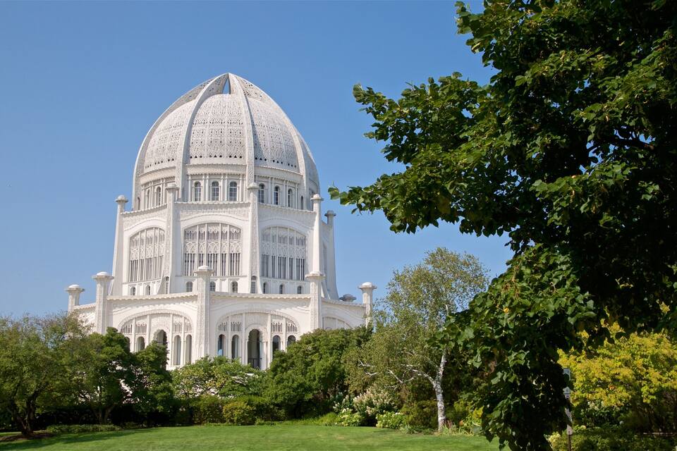 Un edificio grande de color blanco con una cúpula, rodeado de árboles y césped.