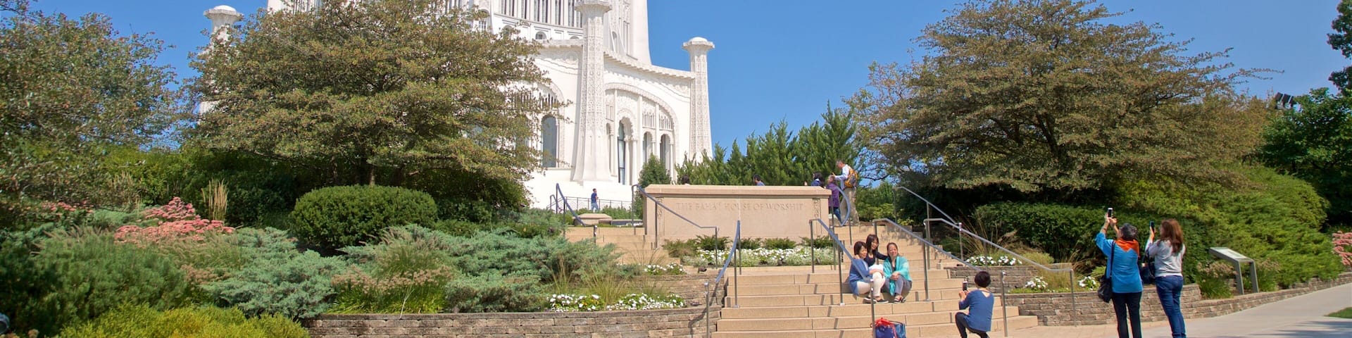 A large white building with intricate designs, surrounded by greenery and a clear blue sky.