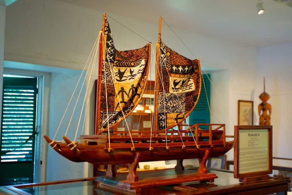 Ein detailliert gestaltetes hölzernes Schiffsmodell mit Segeln, präsentiert in einem Museumsambiente.