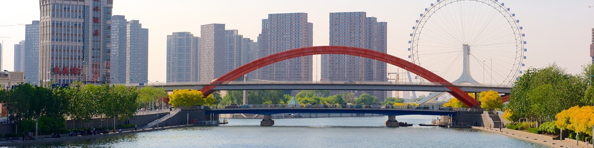 A river with a red bridge, a Ferris wheel, and modern buildings in the background.