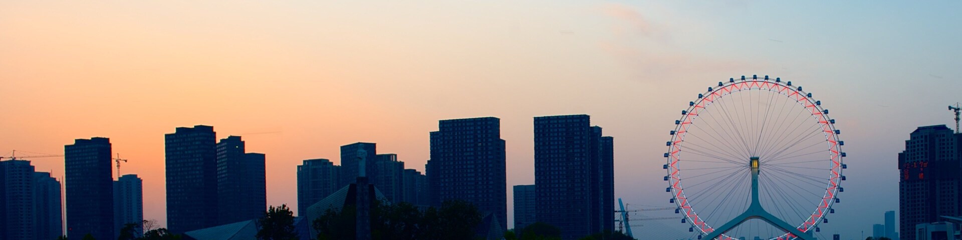 Un horizonte urbano al anochecer, con una noria destacada y modernos rascacielos.