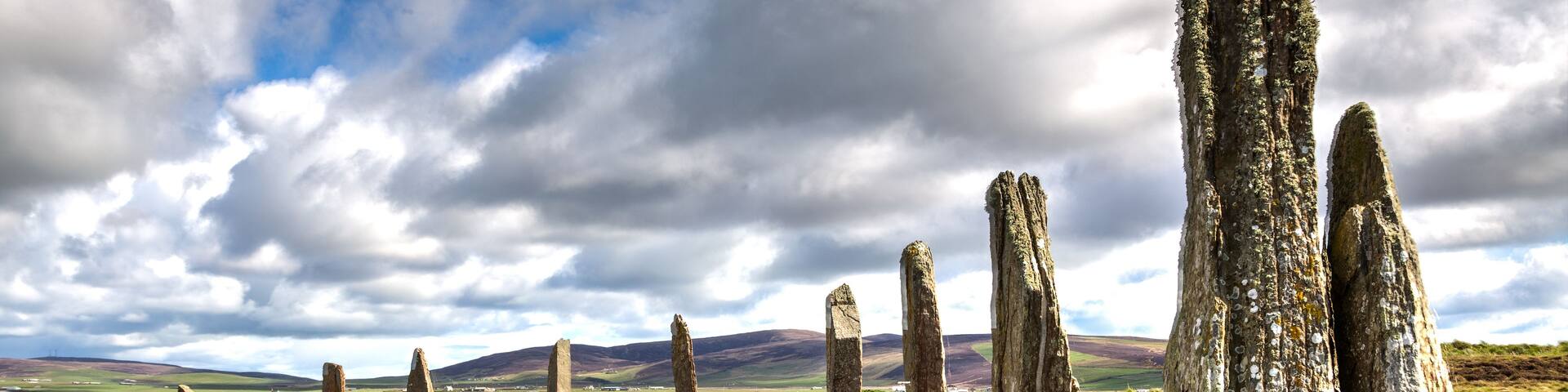 A landscape with standing stones, grassy terrain, and a cloudy sky.