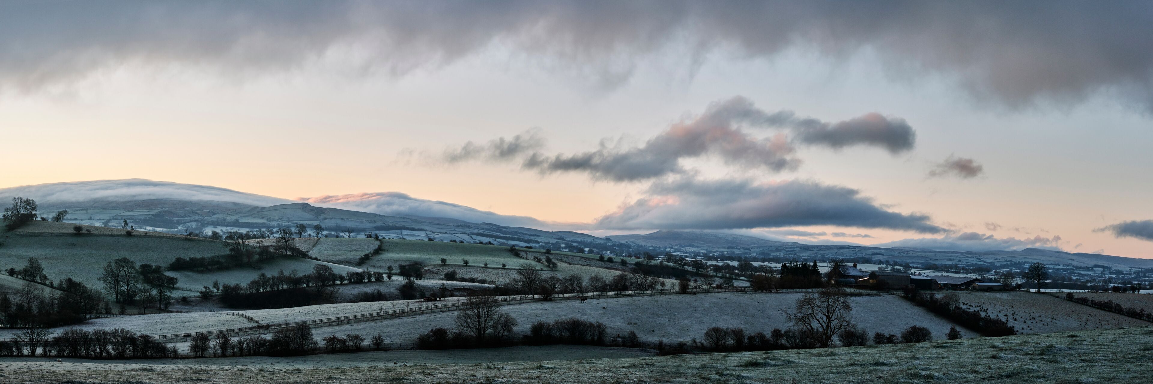 A rural landscape with rolling hills, a distant mountain range, and a small village.