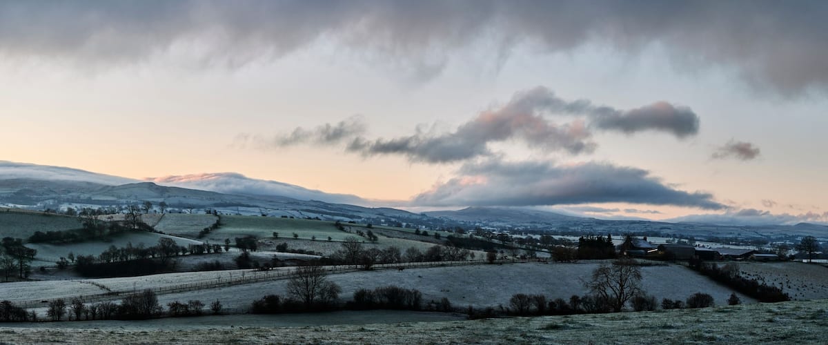 A rural landscape with rolling hills, a distant mountain range, and a small village.