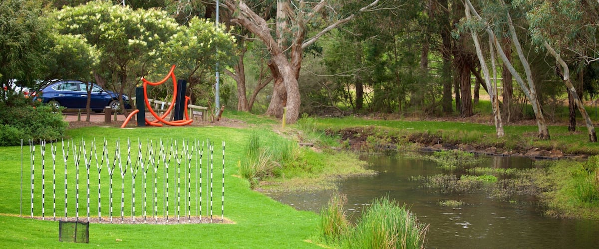 A park with a pond, trees, and exercise equipment.