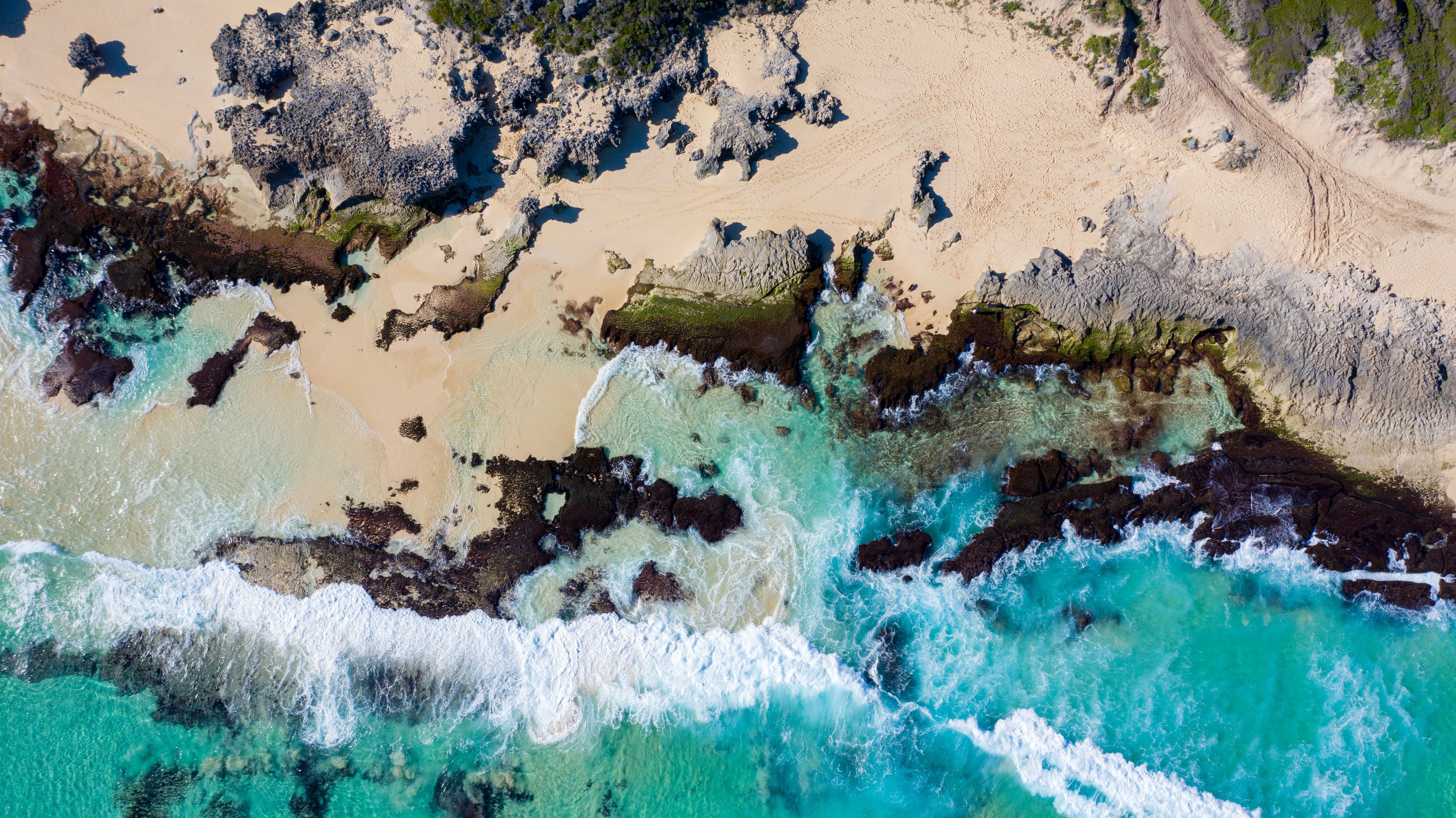 Vue aérienne d’une zone côtière avec des eaux turquoise limpides, des affleurements rocheux et des plages de sable.