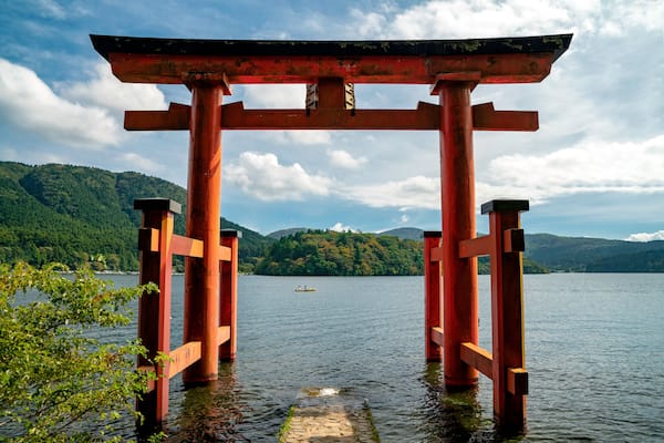 Un portail torii rouge traditionnel, dressé au milieu d’une étendue d’eau, avec une île boisée en arrière-plan.