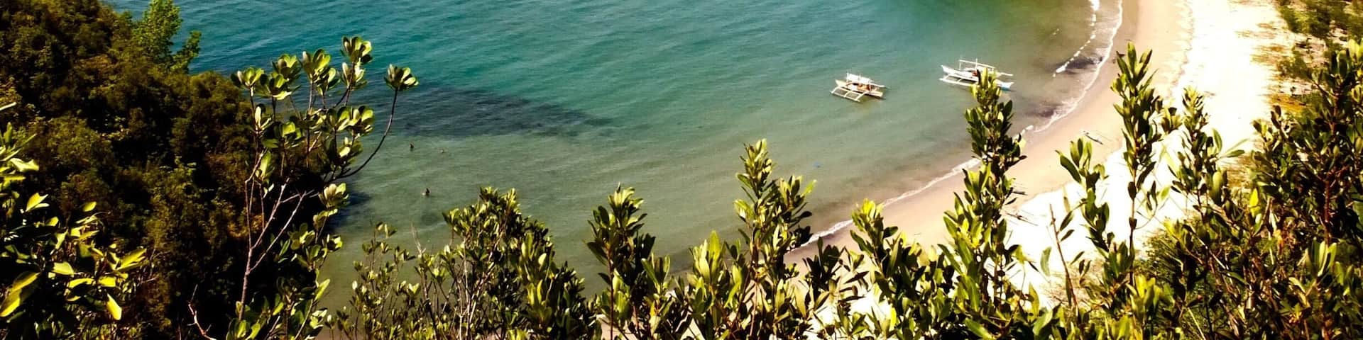 A coastal landscape with a beach, clear blue waters, and surrounding greenery.