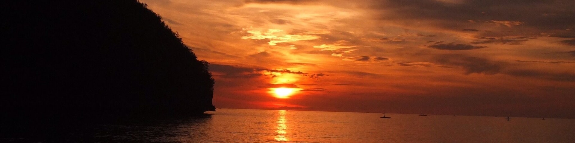 Un atardecer sobre una playa con la silueta de una colina.