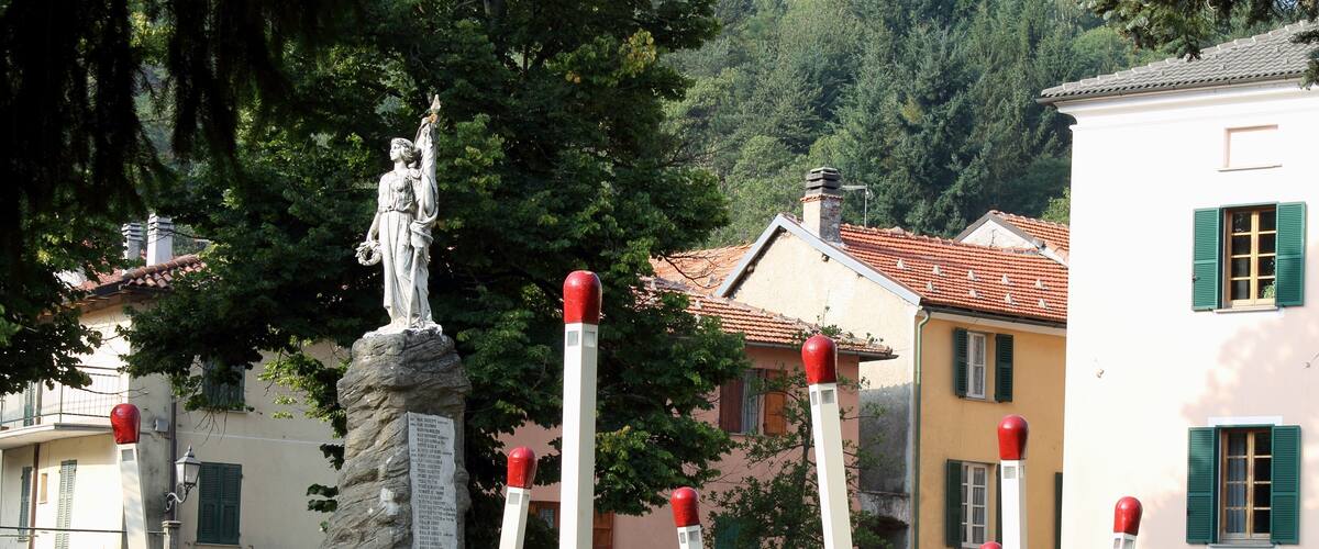 A statue on a pedestal, surrounded by red-topped poles, with buildings and trees in the background.