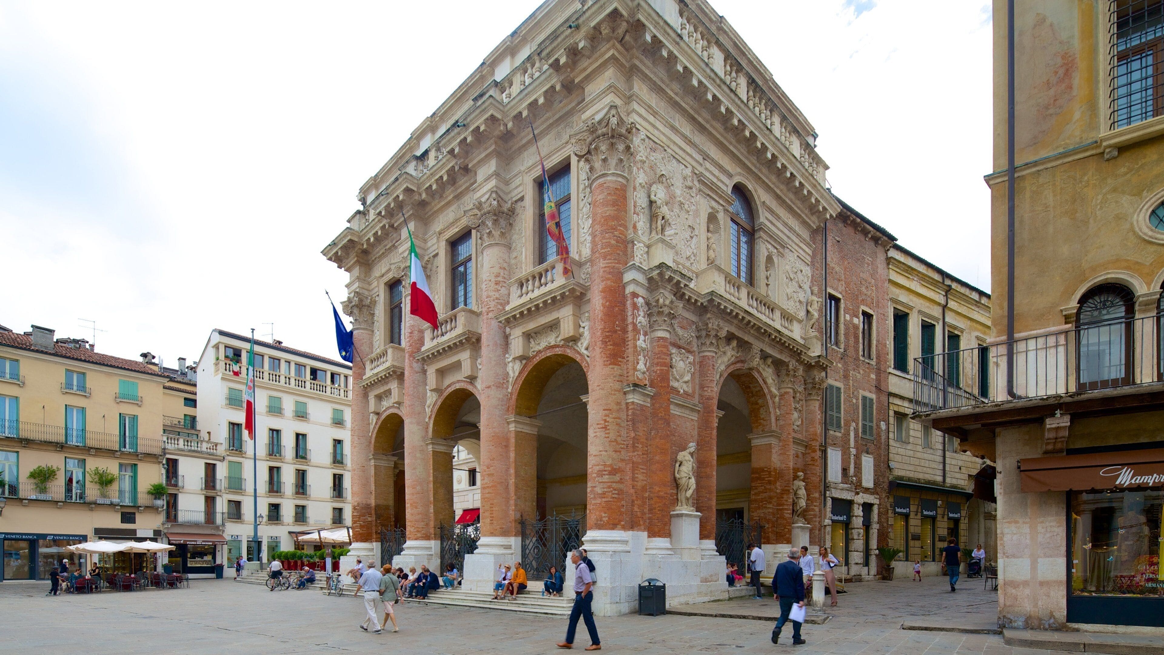 A historic building with ornate architecture, flags, and people in a public square.