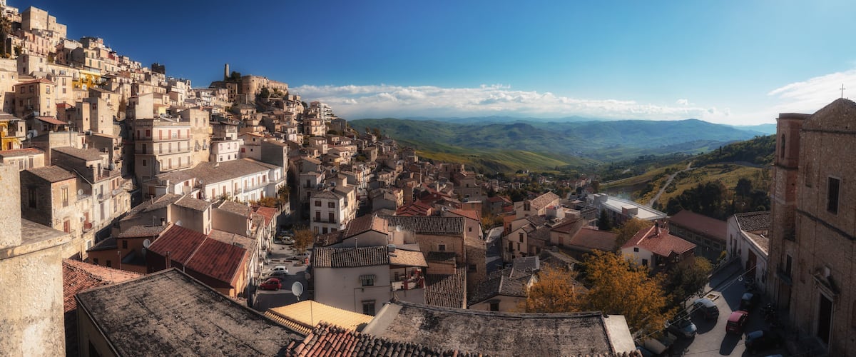 A densely packed hillside town with historic buildings and a view of rolling hills in the distance.