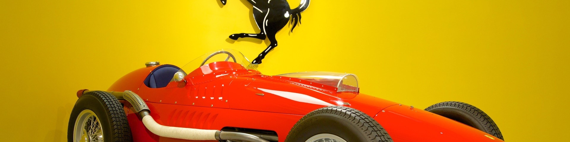 Un coche de carreras antiguo rojo con un logotipo de caballo negro en la pared de fondo.