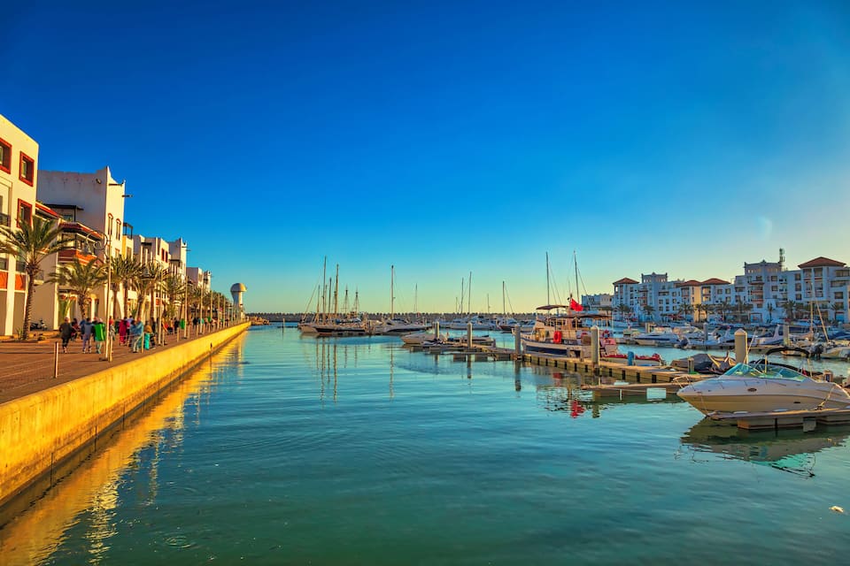 Un port de plaisance avec des bateaux amarrés, une promenade en bord de mer et des bâtiments le long de la côte.