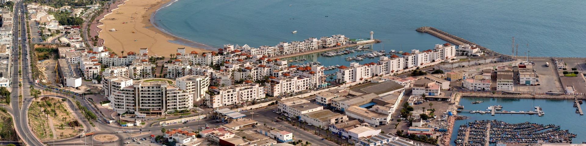 A coastal cityscape with a beach, marina, and dense urban buildings.