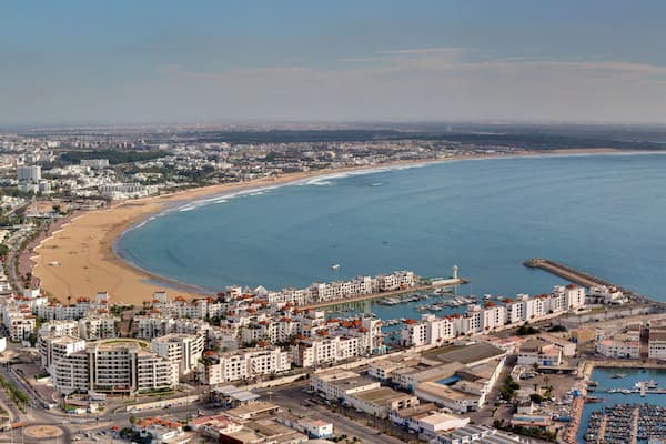 Un paysage urbain côtier avec une plage, un port de plaisance et des bâtiments urbains denses.