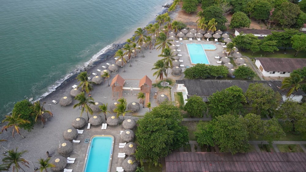 A resort with a swimming pool, beach, palm trees, and a view of the ocean.